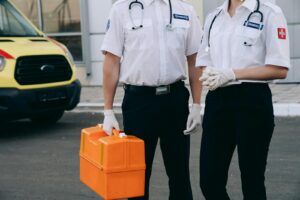 Two paramedics in uniform holding a medical kit next to an ambulance.