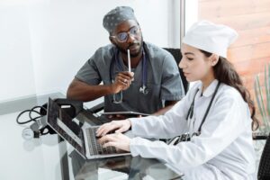 Two doctors discuss patient diagnosis using laptop in hospital office.